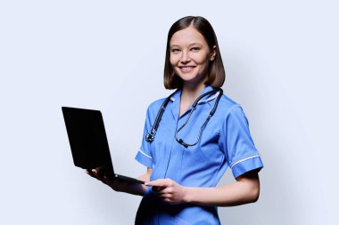 Dizüstü bilgisayarlı gülümseyen genç hemşire portresi beyaz stüdyo arka planında kameraya bakıyor. Tıbbi hizmetlerdeki uygulamalar, sağlık hizmetleri, sağlık hizmetleri, tıbbi yardım