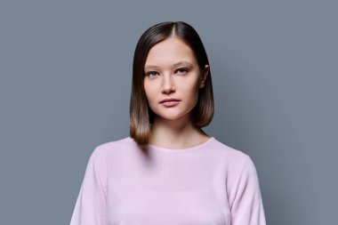 Gri stüdyo arka planında güzel bir kadının portresi. 20 'li yaşlarda kadın kameraya bakıyor. Yaşam tarzı, bakım moda güzellik stili, iş, iş, hizmet, eğitim, gençlik
