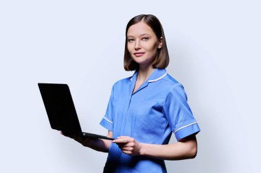 Dizüstü bilgisayarlı gülümseyen genç hemşire portresi beyaz stüdyo arka planında kameraya bakıyor. Tıbbi hizmetlerdeki uygulamalar, sağlık hizmetleri, sağlık hizmetleri, tıbbi yardım