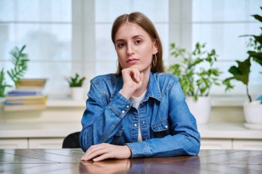 Genç bir kızın portresi. Üniversite öğrencisi. Masada, evde oturan kameraya bakıyor. Gençler, yaşam tarzı, eğitim, öğrenme kavramı