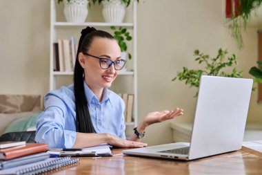 Merkez ofisteki bilgisayarda çalışan orta yaşlı kulaklıklı bir kadın web kamerasına bakarak konuşuyor. Çevrimiçi toplantı, uzak çalışma finansal danışmanlık danışmanlık blog yazarlığı, zihinsel terapi