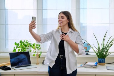 Evde akıllı telefonu olan genç bir kadın görüntülü konuşma yapıyor. Gülümseyen kadın arkadaşlarıyla sosyal ağlarda sohbet ediyor, habercilerle, yaşam tarzıyla, online teknolojilerle iletişim kuruyor.