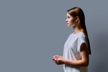 Kızıl saçlı güzel bir kızın profil portresi, gri stüdyo arka planı. Reklam boşluğuna bakan genç bir kadın. Moda güzellik eğitimi için ürünler ve hizmetler