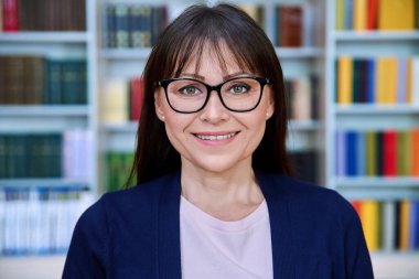 Kütüphanedeki kendine güvenen olgun iş kadınının portresi. Orta yaşlı, gözlüklü zarif bir kadın, yönetici akıl hocası psikolog danışman kütüphane danışmanı kitaplarla dolu arka plan kitapları.