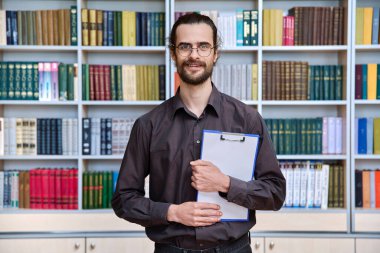 Genç yakışıklı erkek portresi, ofisinde bir panoyla kitap raflarıyla, 30 'larda öğretmen akıl hocası psikolog okul danışmanı kameraya bakan sosyal hizmet görevlisi, sınıf kütüphanesi içinde.