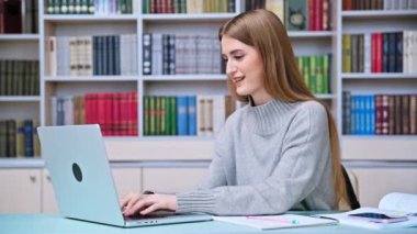 Eğitim kütüphanesinde okuyan genç kız öğrenci dizüstü bilgisayarında daktilo kullanıyor. Eğitim, ergenlik, lise, üniversite, bilgi, öğrenim, teknoloji kavramı