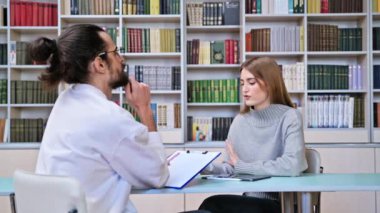 Genç kız öğrenci, genç erkek öğretmen akıl hocası sosyal hizmetler danışmanıyla ofis kütüphanesinde birlikte oturuyor. Psikoloji, akıl sağlığı, eğitim, eğitim, gençlik kavramı