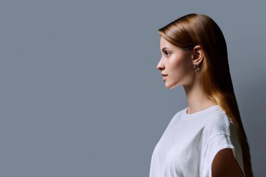 Kızıl saçlı güzel bir kızın profil portresi, gri stüdyo arka planı. Reklam boşluğuna bakan genç bir kadın. Moda güzellik eğitimi için ürünler ve hizmetler