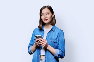 Beyaz arka planda akıllı telefon kullanan mutlu genç bir kadın. Gülümseyen 20 'li yaşlarda bir kadın kameraya mesaj atıyor. Mobil İnternet uygulamaları iş eğitimi iletişim alışverişi için başvuru teknolojileri