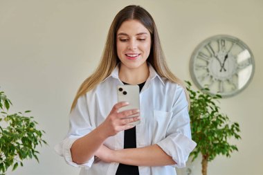 Duvarın yanında duran akıllı telefonu kullanan genç bir kadın. Kadın mesajlaşması okuma, mobil uygulama teknolojisi iş eğitimi için internet hizmetleri eğlence iletişim alışveriş yaşam tarzı