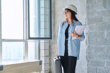 Bayan mimar portresi. Son model dekoratör. Yeni ofis onarım müdürü. Kasklı gülümseyen bir kadın, elinde bir çanta dolusu ekipman, çizim planları pencereye bakan, kopyalayan...