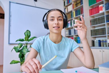 Webcam 'de genç kız, lise öğrencisi, kulaklıklı, kamerayla konuşan. Uzaktan çalışan kız öğrenci, video konferans sohbeti, online sınav dersi. Teknoloji eğitimi gençliği