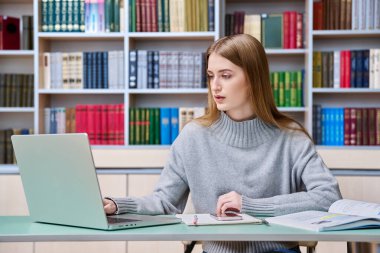 Eğitim kütüphanesinde okuyan genç kız öğrenci dizüstü bilgisayar kullanıyor. Eğitim, ergenlik, lise, üniversite, bilgi, öğrenim, teknoloji kavramı
