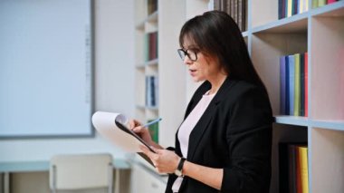 Olgun bir iş kadını, kütüphane kitaplığı raflarıyla ofis içi panolarına yazı yazıyor. Kendine güvenen orta yaşlı kadın psikolog öğretmen sosyal hizmet görevlisi iş yerinde çalışan