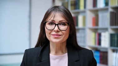 Kütüphanedeki kendine güvenen olgun iş kadınının portresi. Orta yaşlı, gözlüklü zarif bir kadın, yönetici akıl hocası psikolog danışman kütüphane danışmanı kitaplarla dolu arka plan kitapları.