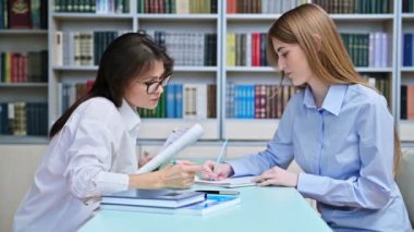 Genç kız öğrenci kütüphane raflarıyla birlikte sınıfın içinde bayan öğretmen eğitmen eğitmeniyle çalışıyor. Eğitim, ergenlik, lise, üniversite, bilgi, öğrenim kavramı