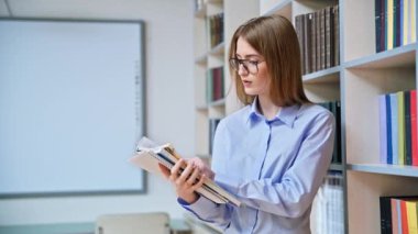 17-18 yaşlarında genç bir kızın portresi. Sınıf kütüphanesinde ders kitaplarını tutuyor. Gözlüklü sarışın genç kadın, eğitim kitaplarıyla dolu raflar.