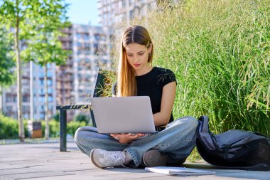 Genç ve çekici bir üniversite öğrencisi bilgisayarla dışarıda bilgisayar kullanıyor, modern şehir geçmişi var. Eğitim, teknoloji, eğitim, 17-18 yaş gençlik kavramı