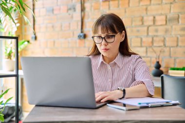 Orta yaşlı iş kadını başarılı ciddi bir kadının birlikte çalıştığı kafede dizüstü bilgisayarla uzaktan kumandayla çalıştığına inanıyor. İş, olgun insanlar, başarı, liderlik, yönetim, güçlendirme kavramı