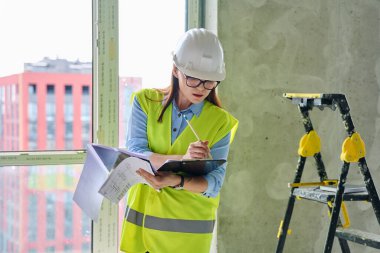 Güvenlik kasklı teknik uzman kadın inşaat işinde çalışıyor. Kendine güvenen endüstriyel kadın mühendis müfettişi müfettiş müteahhit mimarı planlar çizen planlar çizen bir mimar