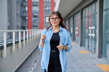 Açık havada gülümseyen, kendine güvenen olgun bir kadının şehir arka planında çekilmiş bir portresi. Yaşam tarzı, orta yaş, iş, iş, insan kavramı