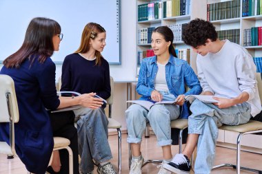 Bir grup genç öğrenci, sınıf kütüphanesinde kadın akıl hocası psikolog danışmanıyla birlikte oturuyor. Lise eğitimi takım çalışması davranış öğrenme konsepti