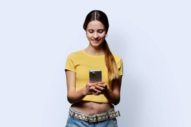 Beyaz stüdyo geçmişinde akıllı telefon kullanan genç ve güzel bir kadın. Moda tebessümü olan kızıl saçlı bir kadın cep telefonuna bakıyor. Teknolojiler mobil uygulama hizmetleri gençlik kavramı