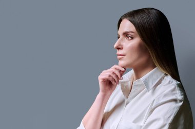 Profil görüntüsü, gri stüdyo arka planındaki genç kadın fotokopi alanı. Beyaz gömlekli, gülümseyen iş kadını boş bir yere bakıyor. Gençlik, eğitim hizmetleri sağlık güzellik işi