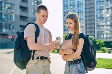 Arkadaşlar, öğrenciler, gülümseyen, konuşan, yürüyen, erkek ve kız 17,18 yaşında, akıllı telefona birlikte bakan, modern şehir, şehir geçmişi. Yaşam tarzı, gençler, üniversite gençlik hayatı konsepti