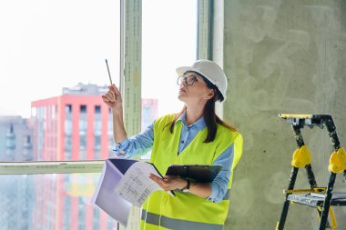 Güvenlik kasklı teknik uzman kadın inşaat işinde çalışıyor. Kendine güvenen endüstriyel kadın mühendis müfettişi müfettiş müteahhit mimarı planlar çizen planlar çizen bir mimar
