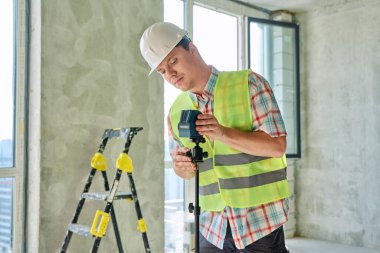 İnşaat alanında güvenlik kasklı, profesyonel ekipman lazer seviyeli genç sanayi işçisinin portresi. İnşaat onarım servisi geliştirme çalışma konsepti