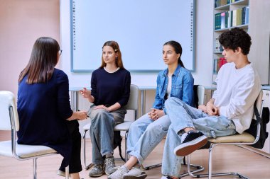 Grup zihinsel terapisi, genç üniversite öğrencileri çemberde oturup kadın psikolog sosyal hizmet danışmanı öğretmeniyle sınıf ofisinde konuşuyor. Ruh sağlığı, eğitim, gençlik