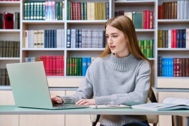 Eğitim kütüphanesinde okuyan genç kız öğrenci dizüstü bilgisayar kullanıyor. Eğitim, ergenlik, lise, üniversite, bilgi, öğrenim, teknoloji kavramı