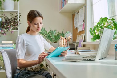 Yaratıcılık, çalışma, dizüstü bilgisayar monitörüne bakmak için grafik tablet kullanan genç bir kız, evde masada oturuyor. Yaratıcılık, öğrenim, teknoloji, eğitim, serbest meslek, gençlik kavramı