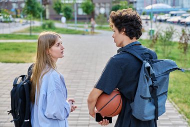 Arkadan manzara, yürüyen arkadaşlar, sırt çantalı kız ve erkek üniversite öğrencileri, modern şehrin caddelerinde birlikte konuşuyorlar. Gençlik, arkadaşlık, iletişim, kentsel yaşam tarzı konsepti