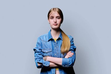 Sarışın, kendine güvenen genç kız kollarını kavuşturup gri arka plandaki kameraya bakıyor. Başarılı genç kız öğrenci üniversite yaşı gençlik için reklam ürünleri ve hizmetleri