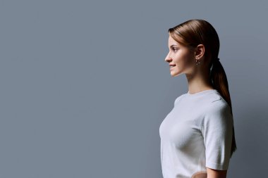 Kızıl saçlı güzel bir kızın profil portresi, gri stüdyo arka planı. Reklam boşluğuna bakan genç bir kadın. Moda güzellik eğitimi için ürünler ve hizmetler