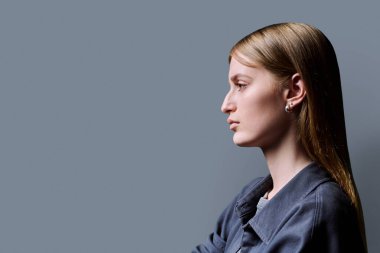 Profil görüntüsü, özgüveni yüksek genç bir kadın gri stüdyo arkaplanını dört gözle bekliyor, reklam metni için kopyalama alanı. Güzel sarışın, moda stili gençlik konsepti.