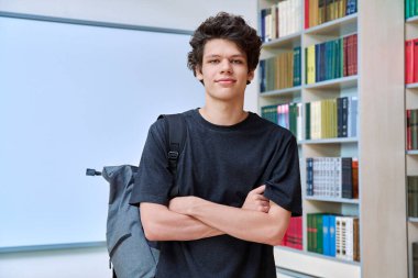 Eğitim binasının kütüphanesinde kollarını kavuşturmuş kendine güvenen yakışıklı üniversite öğrencisinin portresi. Eğitim, gençlik, yaşam tarzı kavramı