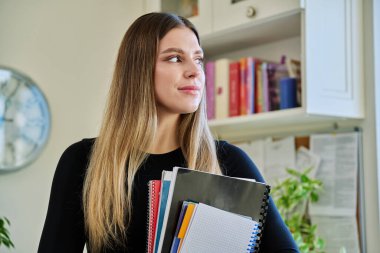 Elinde ders kitapları tutan genç bir üniversite öğrencisinin portresi. Ev içinde, başka yere bakıyor. Eğitim, eğitim, öğrenme, gençlik kavramı