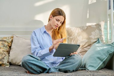 Dijital tabletle kanepede oturmuş evde sınav hazırlığı yapan kız öğrencinin portresi. Gençlik yaşam tarzı eğitim eğlence teknolojisi kavramı