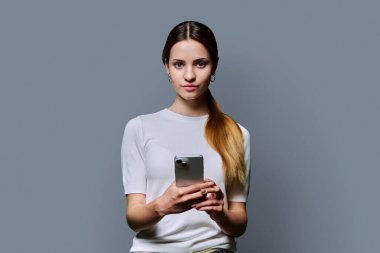 Gri stüdyo geçmişinde akıllı telefon kullanan genç ve güzel bir kadın. Ciddi kızıl saçlı kadın cep telefonuyla kameraya bakıyor. Teknolojiler mobil uygulama hizmetleri gençlik kavramı