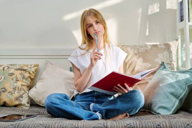 Kız öğrenci portresi elinde not defteriyle kanepede oturuyor, evde sınav için hazırlanıyor. Gençlik yaşam tarzı eğitim kavramı