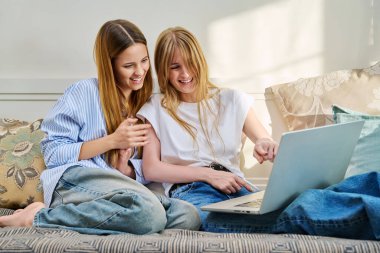 İki neşeli genç kız, kanepede oturan dizüstü bilgisayara bakarak evde üniversite öğrencileri olarak gülüyor. Eğitim öğrenme teknolojisi gençlik arkadaşlığı