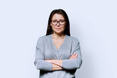 Kollarını çapraz bağlamış, beyaz stüdyo arka planında kameraya bakan olgun, kendine güvenen esmer kadının portresi. Orta yaş, yaşam tarzı, güzellik sağlığı, mesleki kariyer kavramı