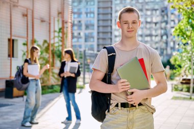 Kendine güveni tam bir üniversite öğrencisi portresi. Sırt çantalı genç bir erkek. Eğitim binasının yakınındaki kameraya bakıyor. Eğitim, eğitim, gençlik kavramı