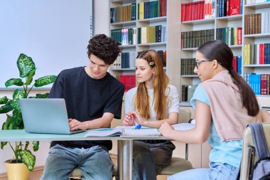 Bir grup üniversite öğrencisi kütüphane sınıfında çalışıyor, sınıf arkadaşları birlikte konuşuyor, takım çalışması projesi, sınavlar ve sınavlar için hazırlanıyor. Eğitim bilgisi ekip çalışması gençlerin iletişimi