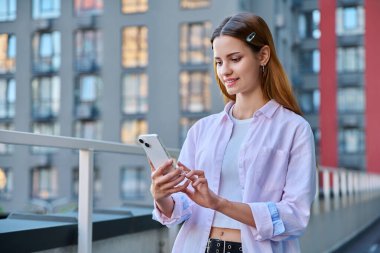 Akıllı telefon kullanan genç bir kadın, modern şehir geçmişi. Ergen öğrenci gezmek için mobil uygulama uygulamaları kullanarak mesajlaşıyor. Teknoloji İnternet Eğitim Gençlik Usulü