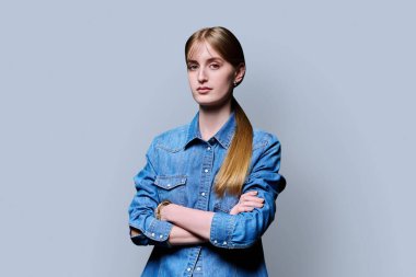 Sarışın, kendine güvenen genç kız kollarını kavuşturup gri arka plandaki kameraya bakıyor. Başarılı genç kız öğrenci üniversite yaşı gençlik için reklam ürünleri ve hizmetleri