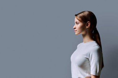 Kızıl saçlı güzel bir kızın profil portresi, gri stüdyo arka planı. Reklam boşluğuna bakan genç bir kadın. Moda güzellik eğitimi için ürünler ve hizmetler